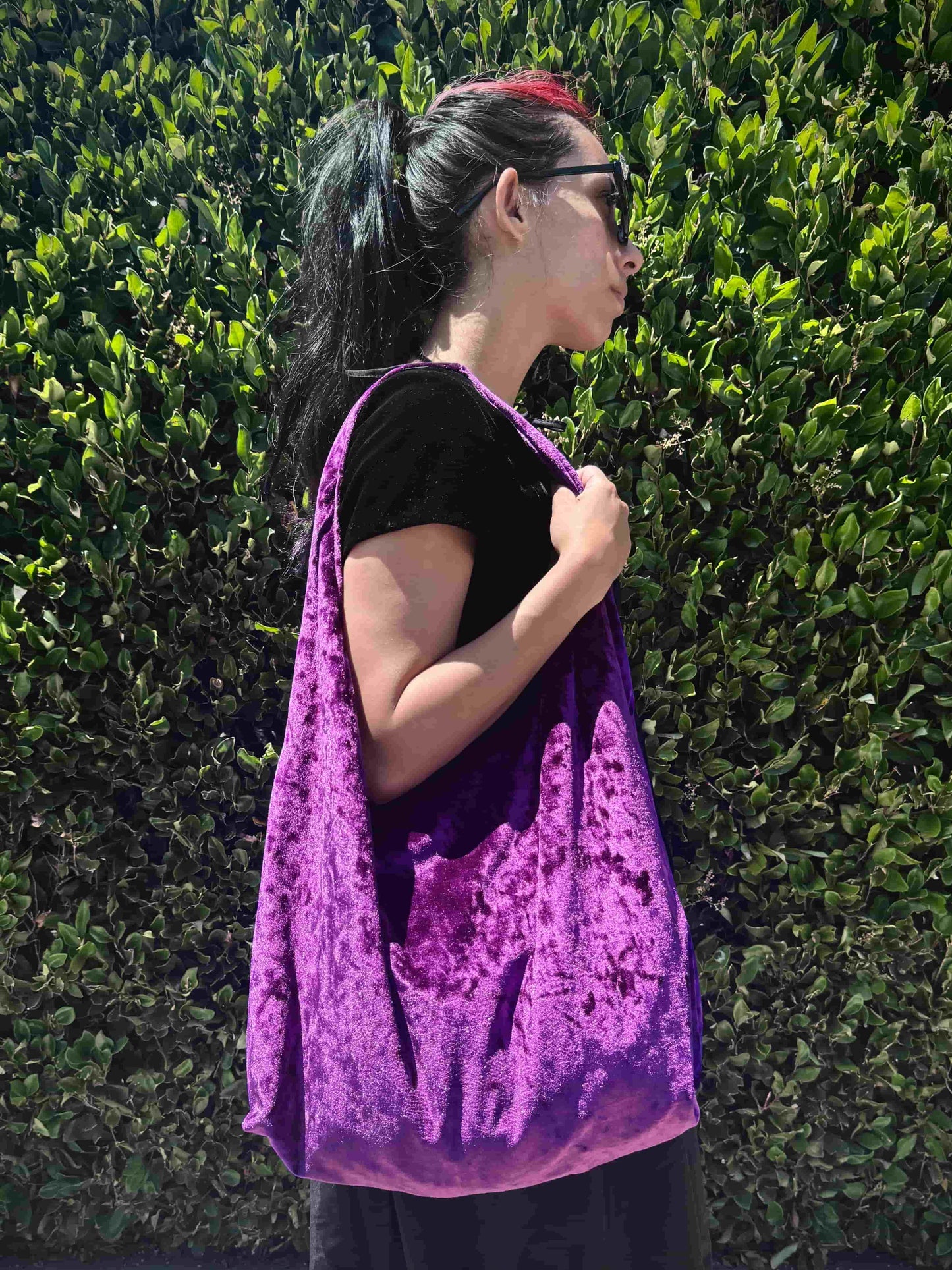 Person wearing a velvet purple bag against a green hedge background