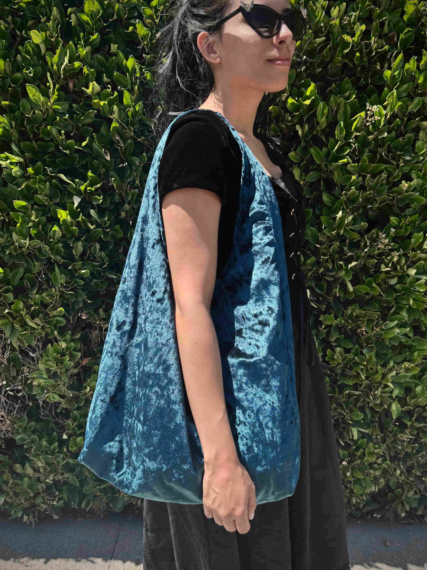 Person wearing a blue velvet bag against a green hedge background
