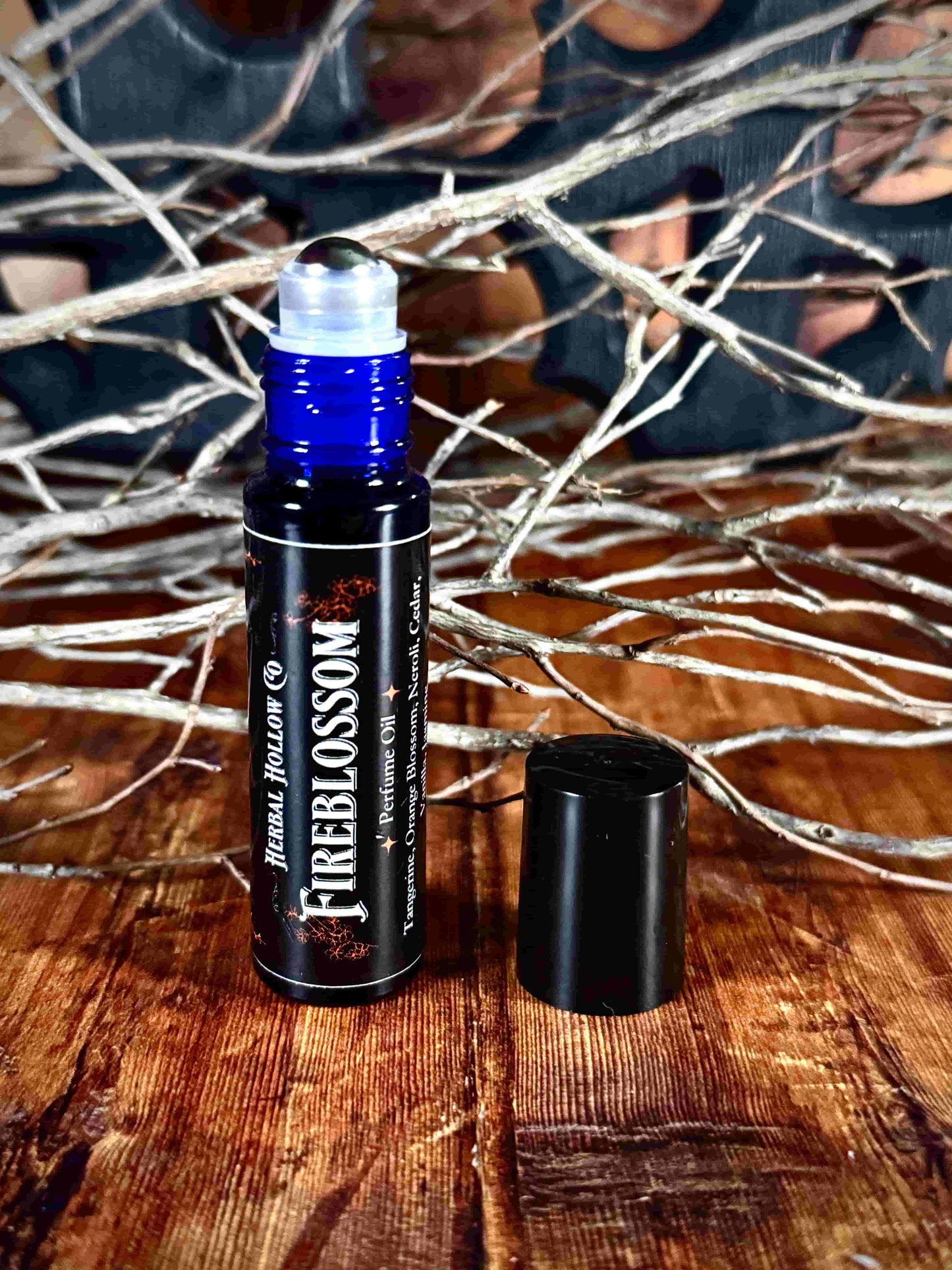 Image of small perfume bottle standing up with cap off. Fireblossom is a fantasy-inspired rollerball fragrance oil perfume, featuring a handcrafted magical neroli, tangerine, bergamot, orange blossom, jasmine, heliotrope, vanilla, cedar, sea salt, and sandalwood scent in a portable glass bottle.