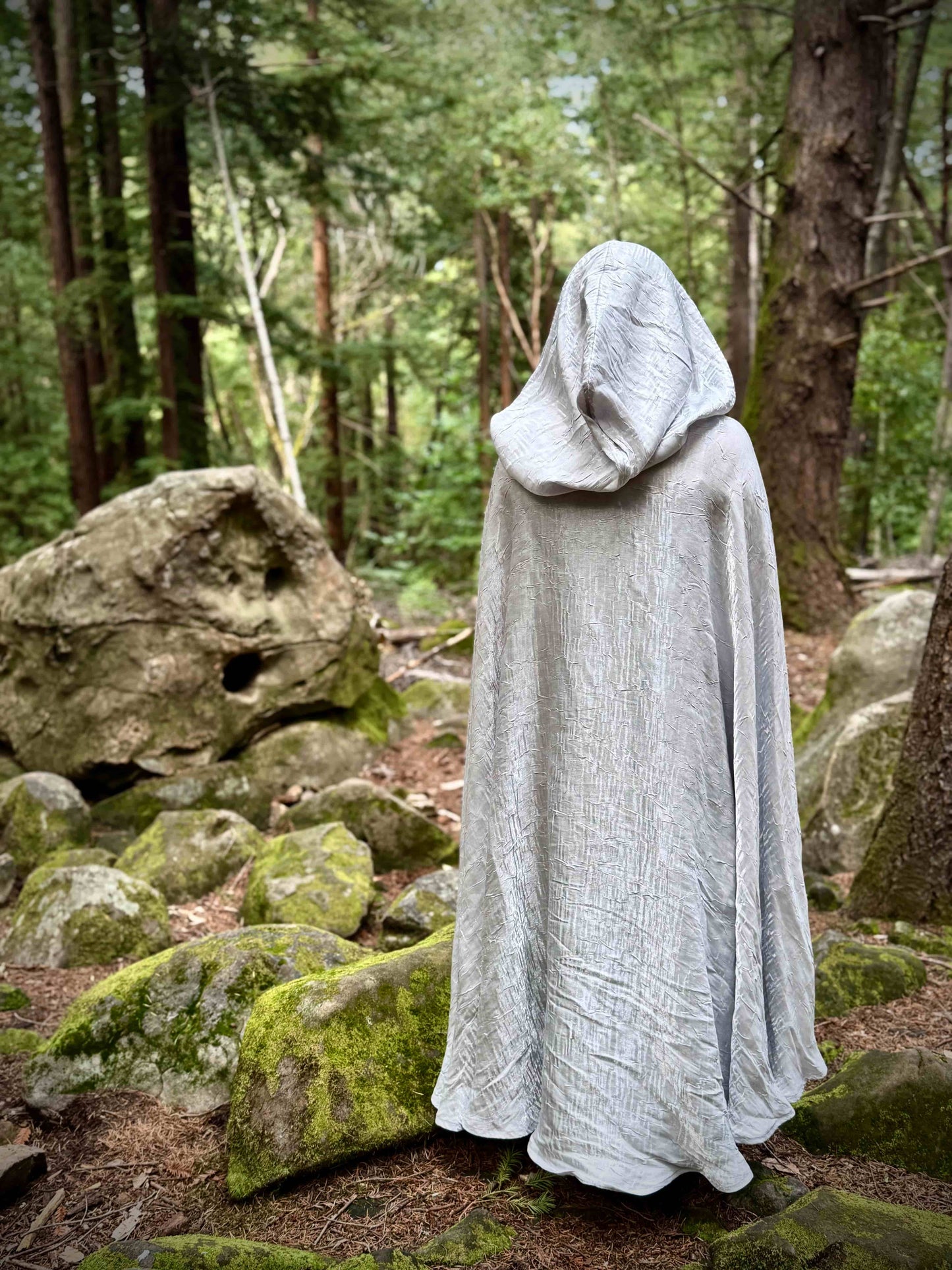 Person in a white hooded cloak standing in a forest setting