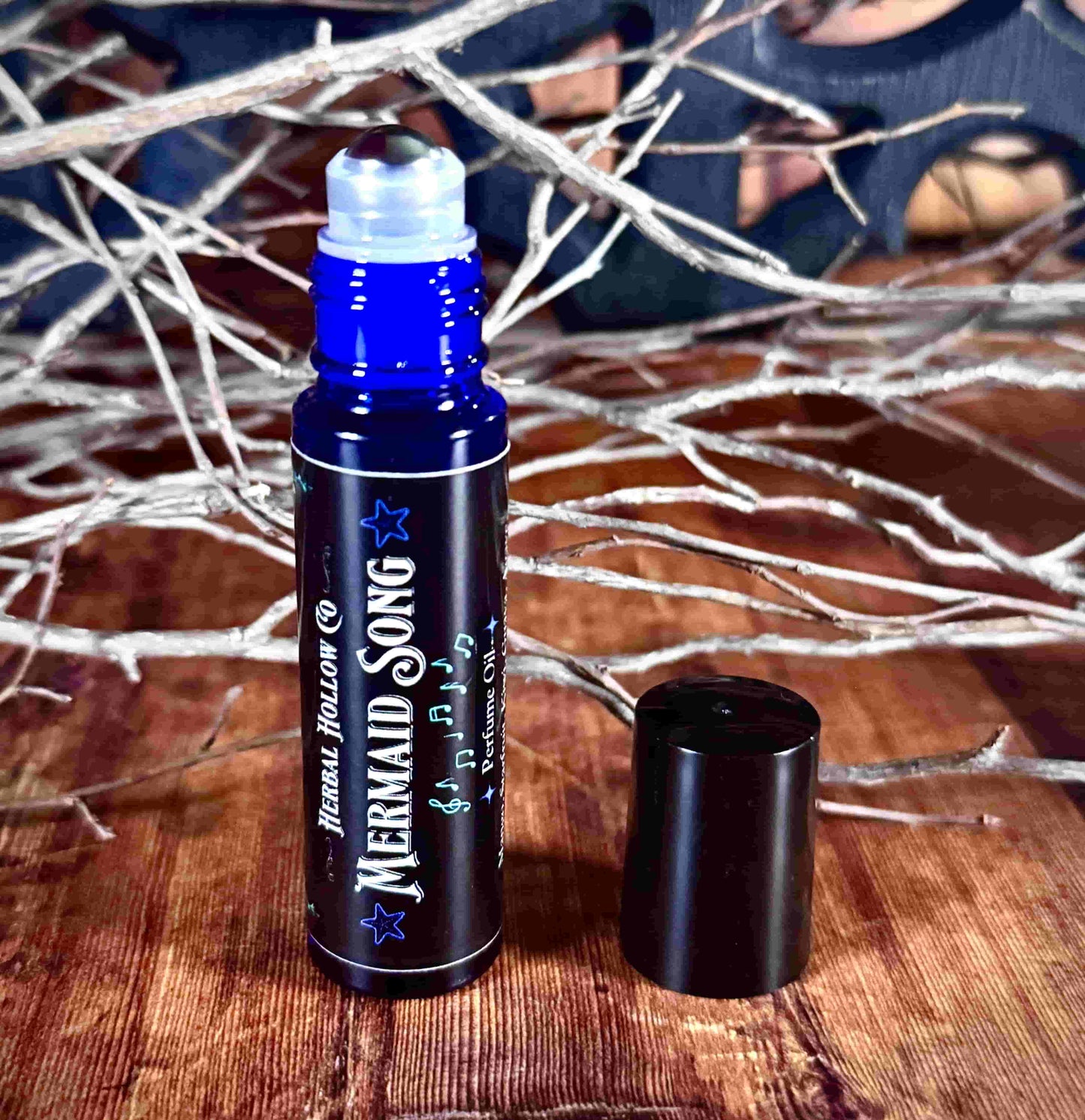 Image of small perfume bottle standing up with cap off. Mermaid Song is a fantasy-inspired rollerball fragrance oil perfume, featuring a handcrafted magical mango, starfruit, kiwi, agave, and guava scent in a portable glass bottle.