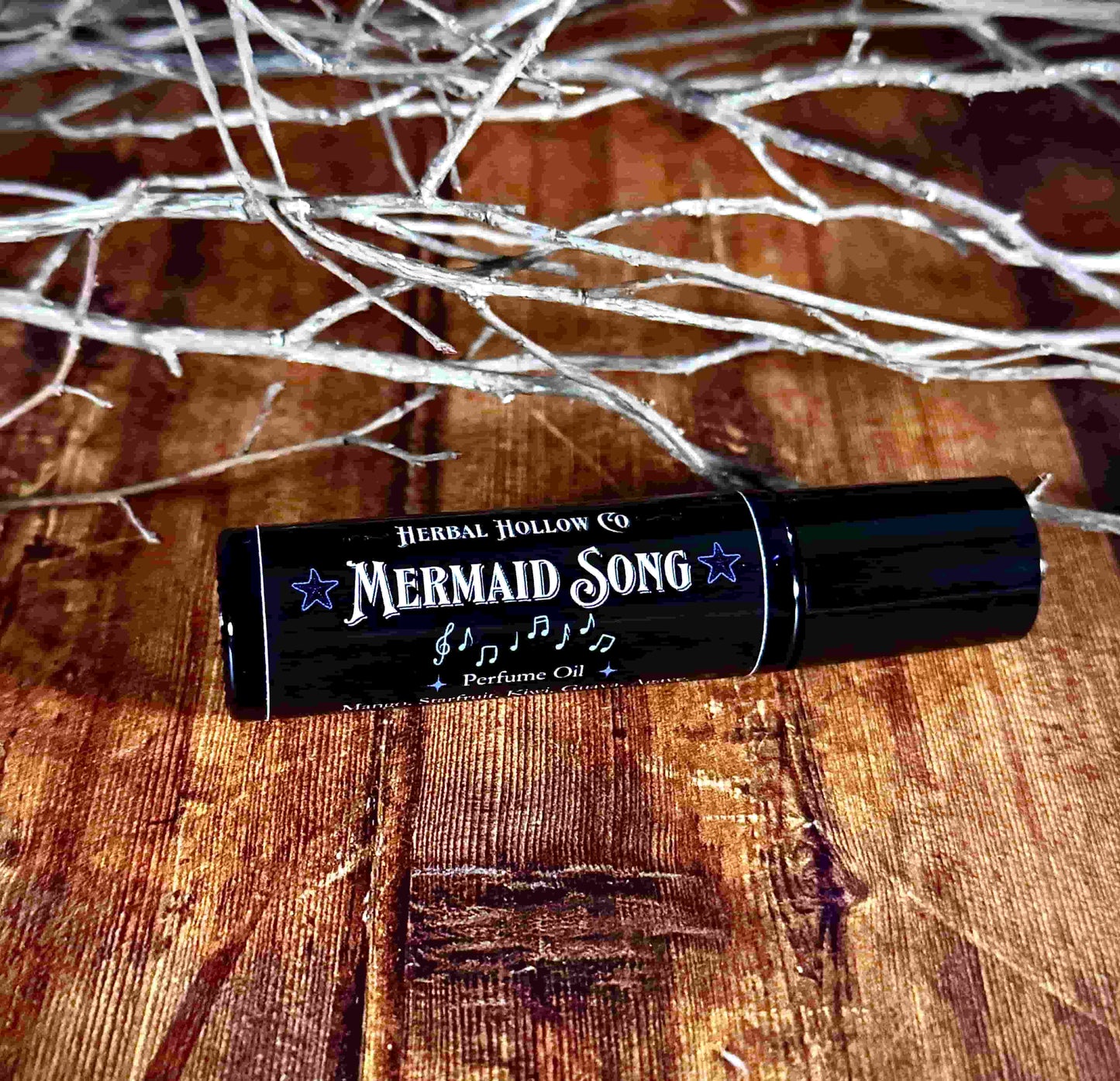 Image of small perfume bottle lying down. Mermaid Song is a fantasy-inspired rollerball fragrance oil perfume, featuring a handcrafted magical mango, starfruit, kiwi, agave, and guava scent.
