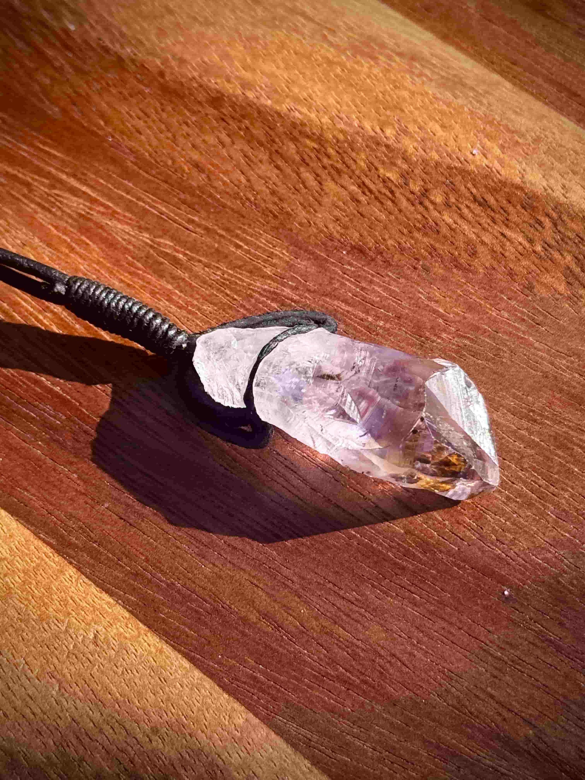 Amethyst stone pendant with inclusions on a leather cord against a wooden table