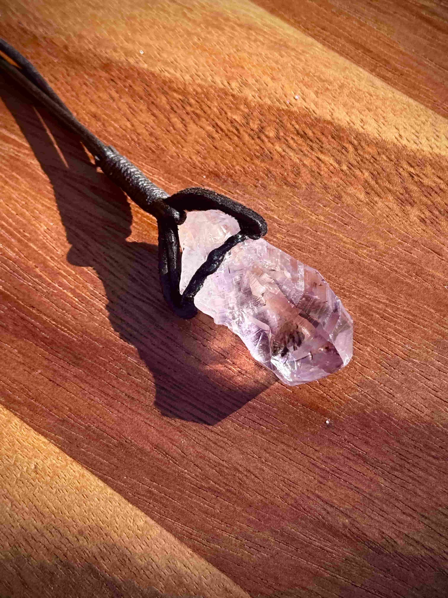 Amethyst stone pendant with inclusions on a leather cord against a wooden background