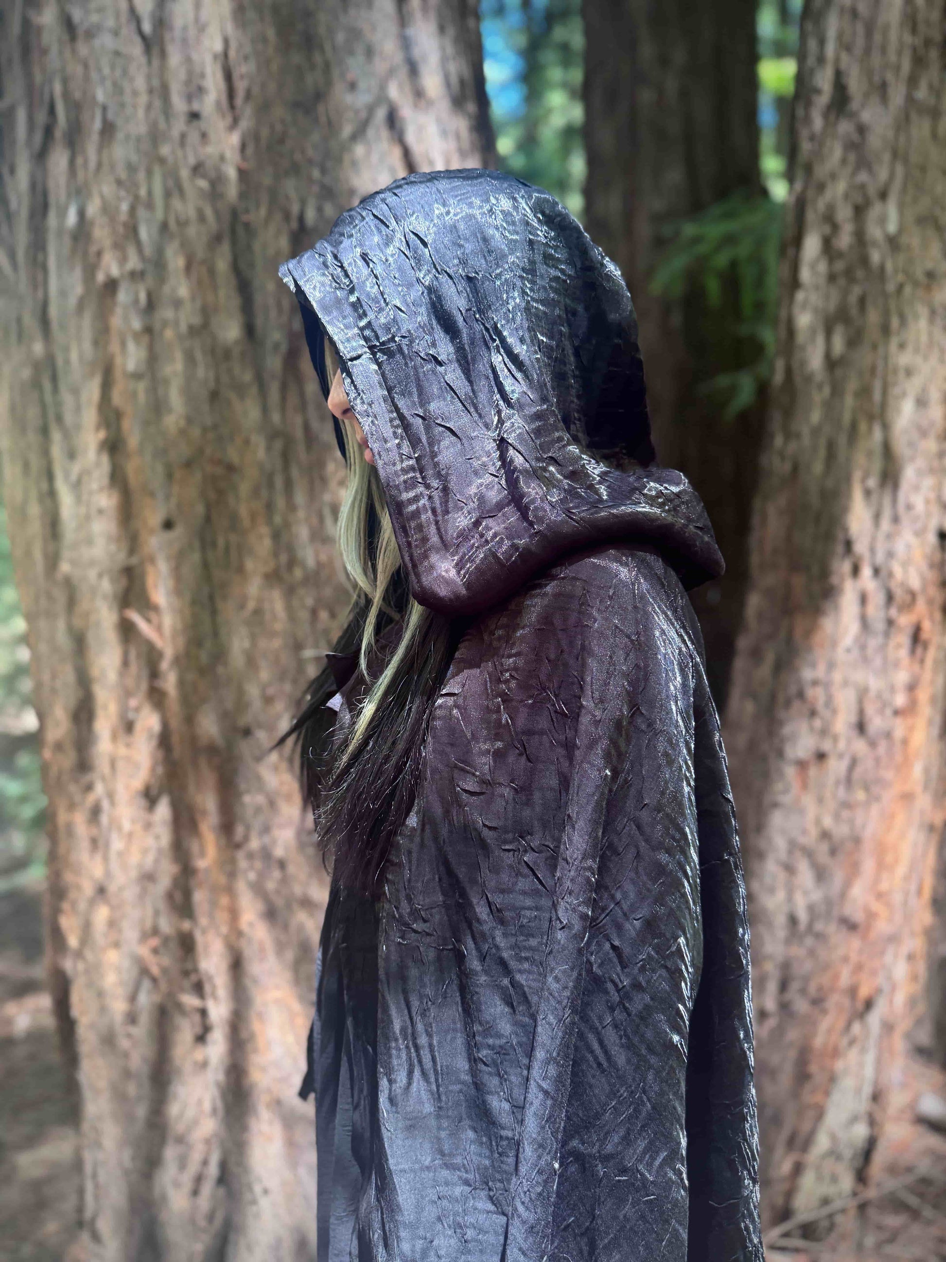 Person wearing a dark hooded cloak in a forest setting