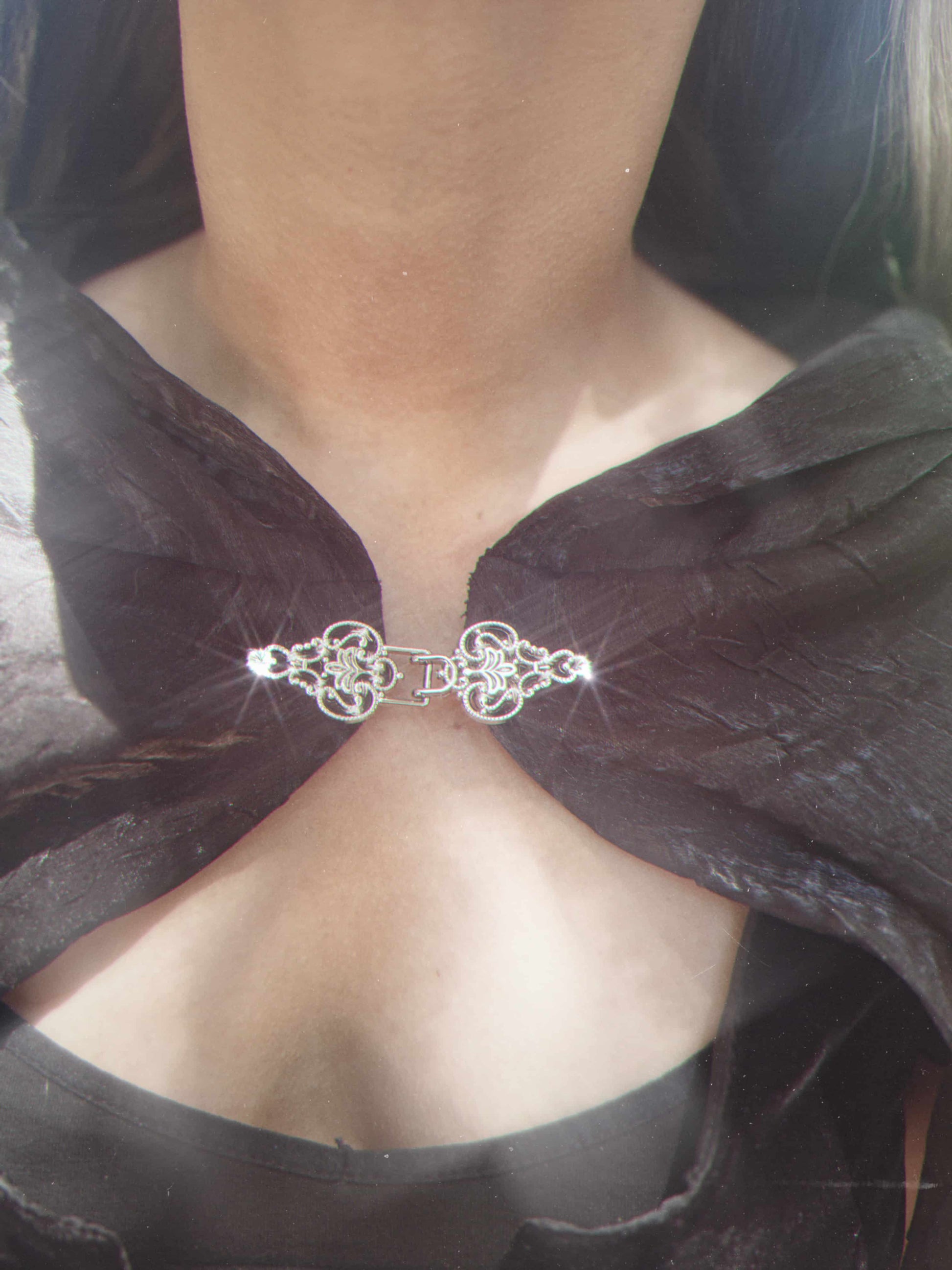 Close-up of a black cape with a decorative silver clasp.