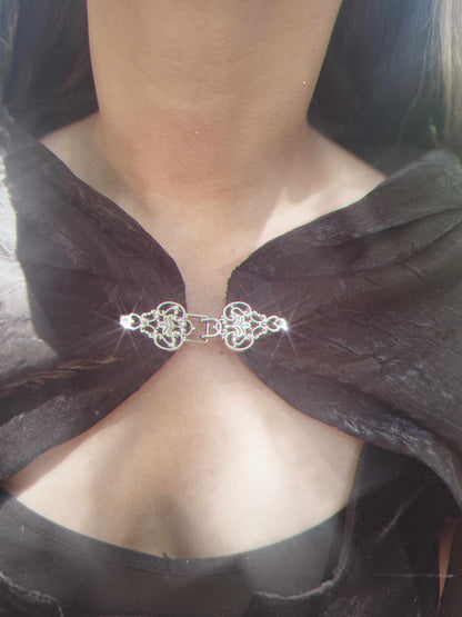 Close-up of a black cape with a decorative silver clasp.