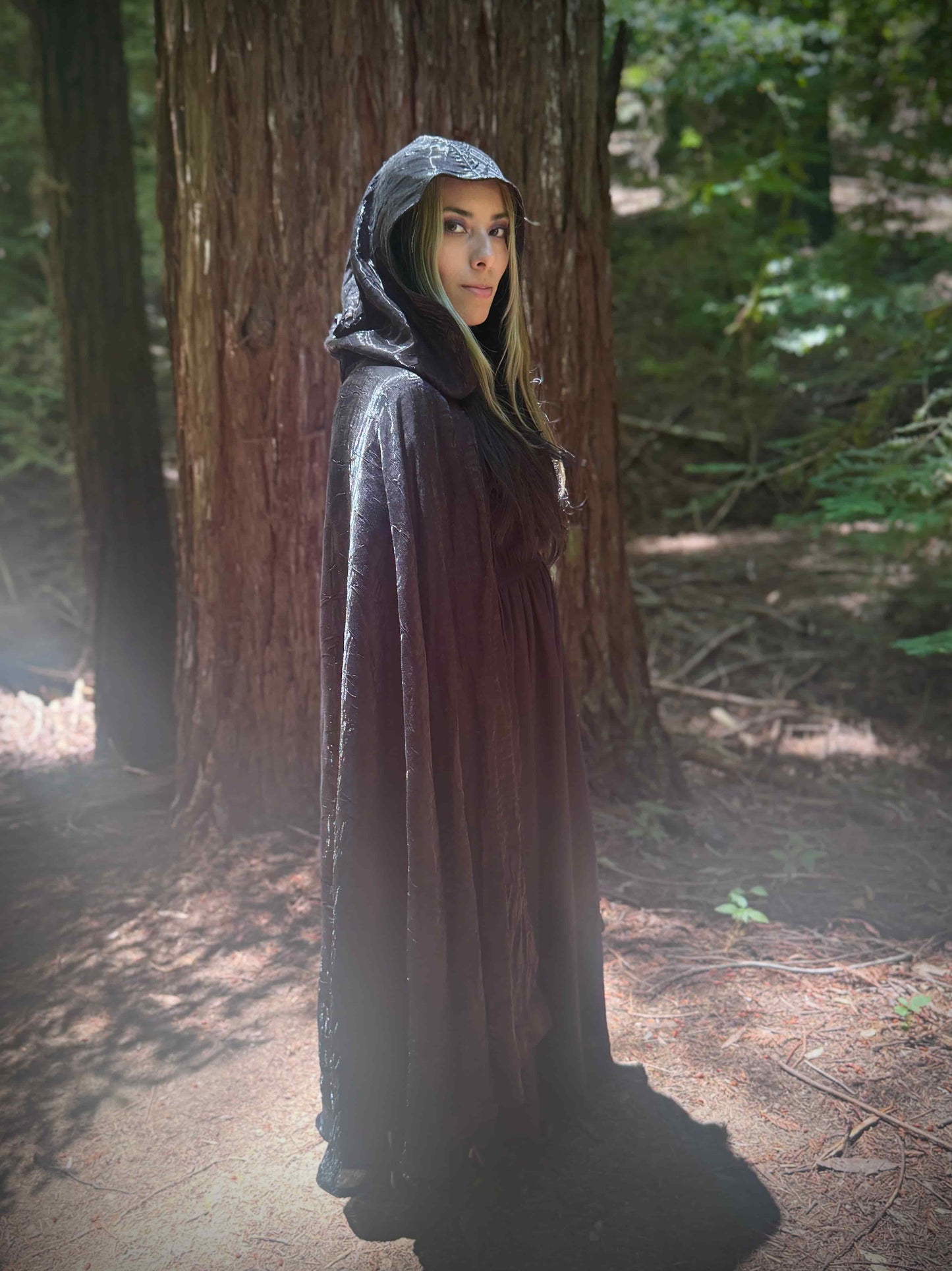 Person wearing a hooded long cloak in a forest setting