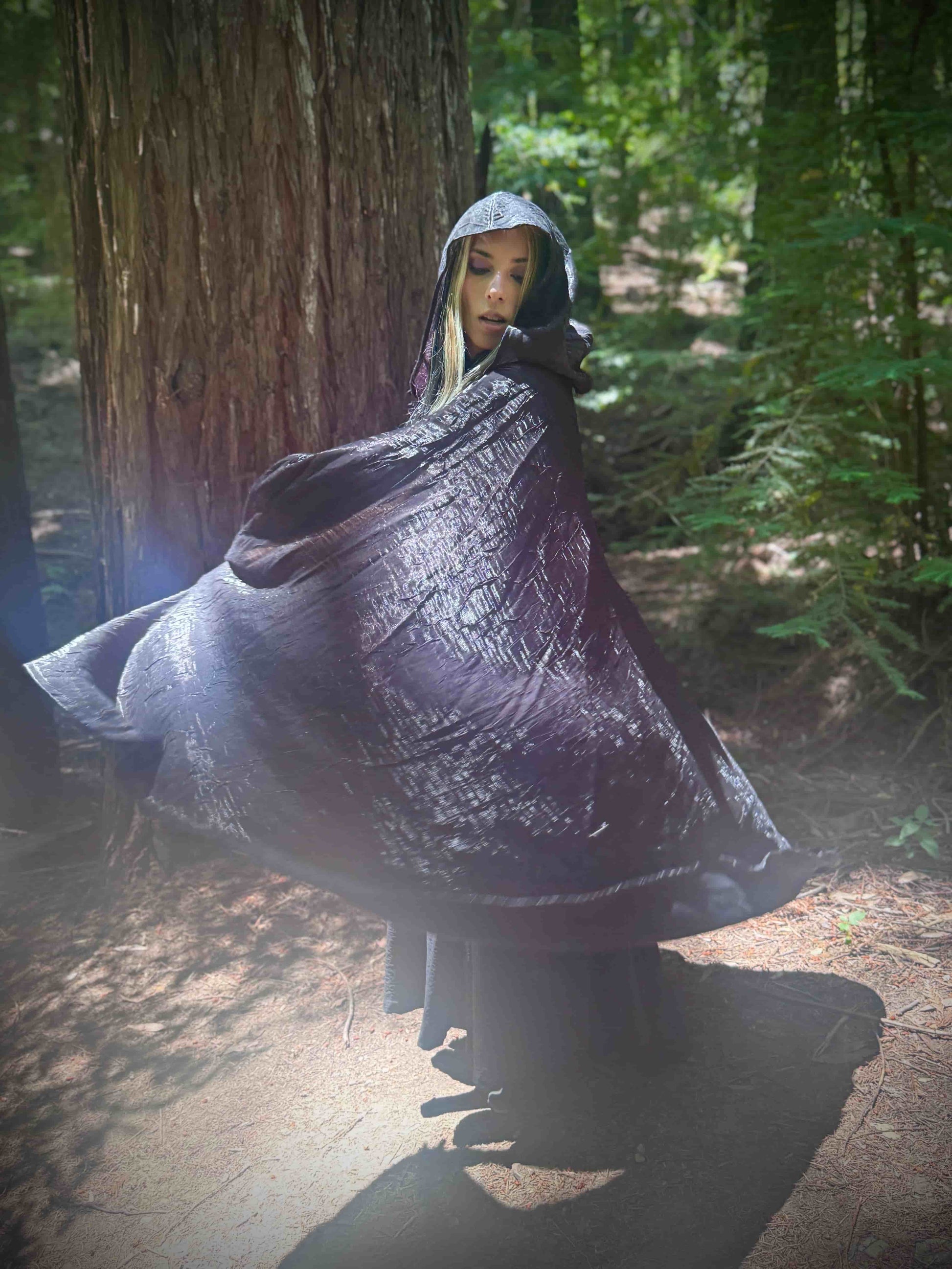 Person wearing a dark black cape in a forest setting, spinning