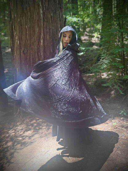 Person wearing a dark black cape in a forest setting, spinning
