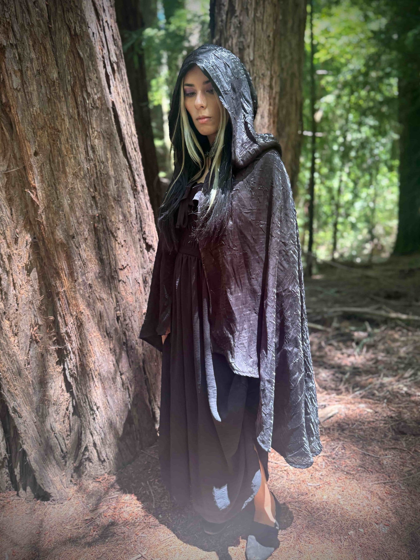 Person wearing a tiered short black hooded cloak in a forest setting