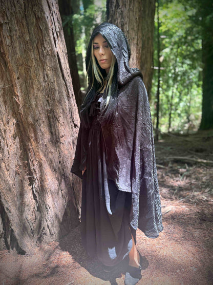 Person wearing a tiered short black hooded cloak in a forest setting