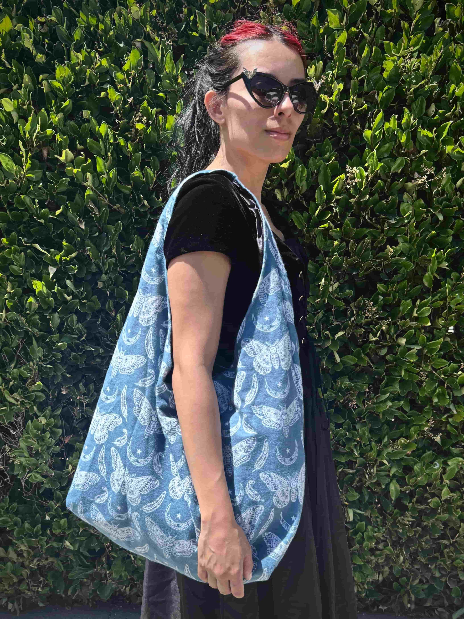 Person wearing a blue and white moth patterned bag against a green hedge background
