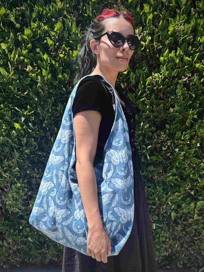 Person wearing a blue and white moth patterned bag against a green hedge background