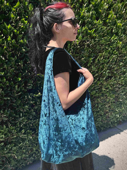 Person wearing a blue velvet bag against a green hedge.