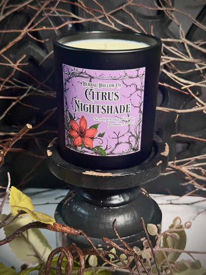 Candle with a 'Citrus Nightshade' label on a decorative stand with branches in the background