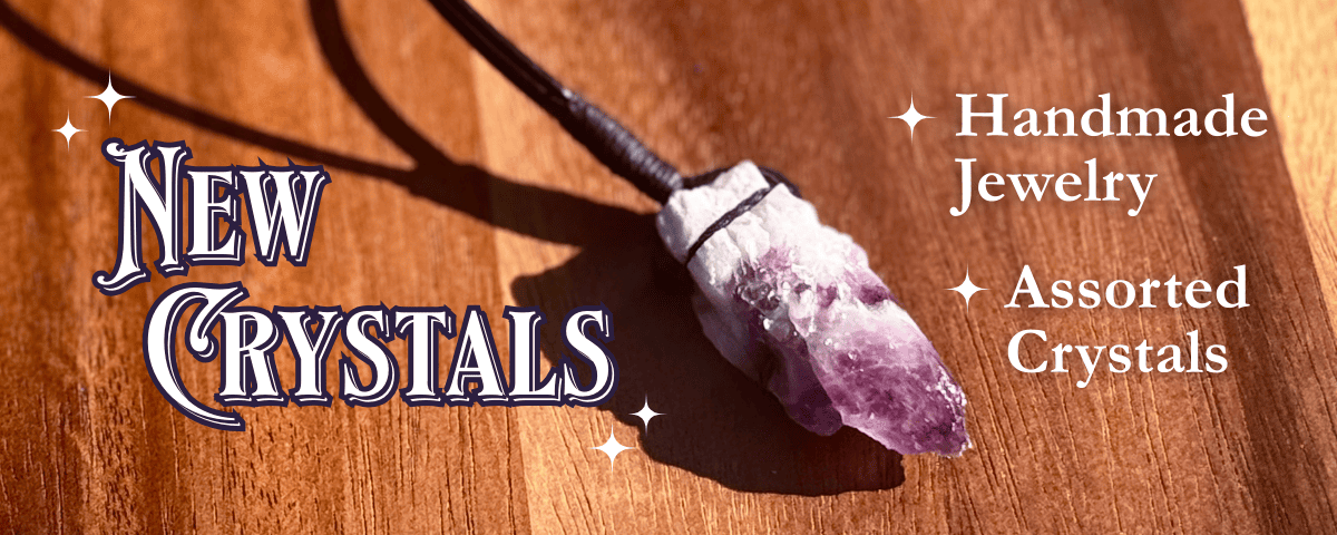Amethyst crystal necklace on a wooden surface with promotional text that reads "New Crystals. Handmade Jewelry. Assorted Crystals," for handmade jewelry and assorted crystals.