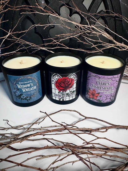 Three candles with gothic floral themed labels on a white surface with branches around