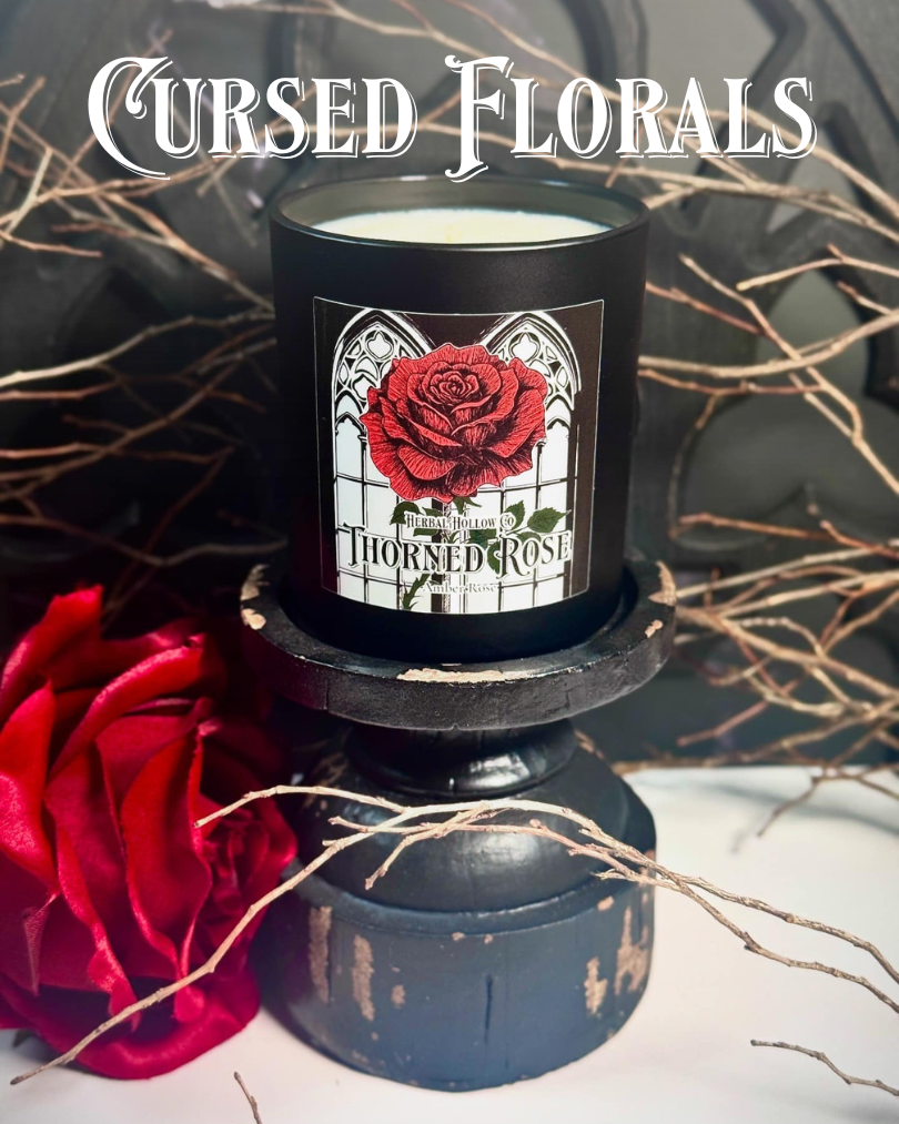 Candle with 'Thorned Rose' design on a decorative stand with red flowers and branches.