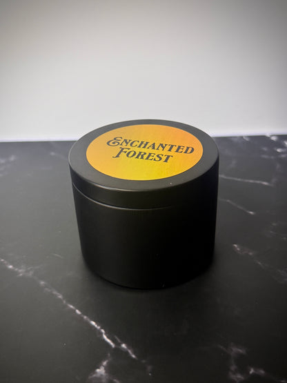 Black tin candle container with 'Enchanted Forest' label on a dark surface