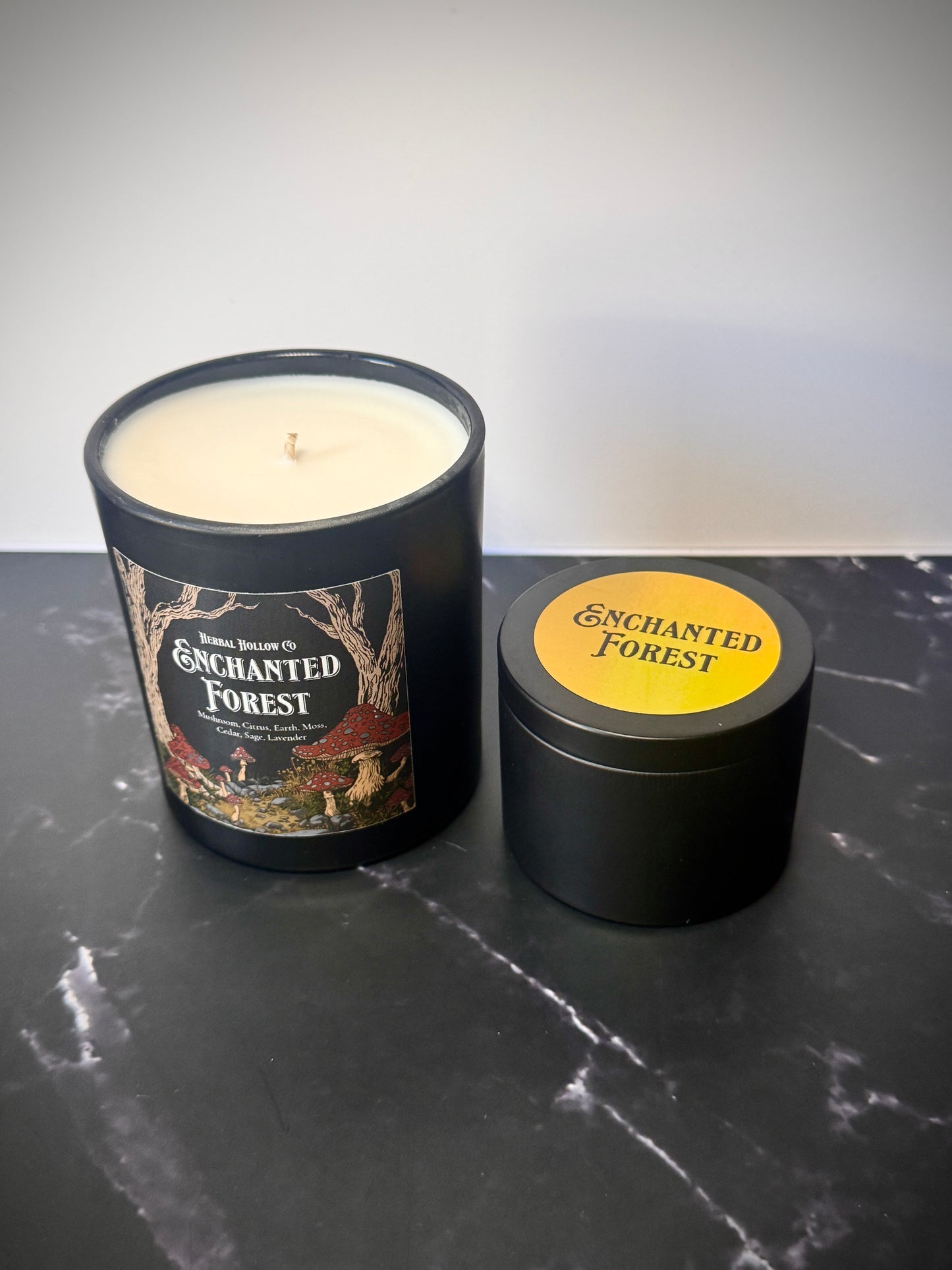 Large and small candles labeled 'Enchanted Forest' on a dark surface
