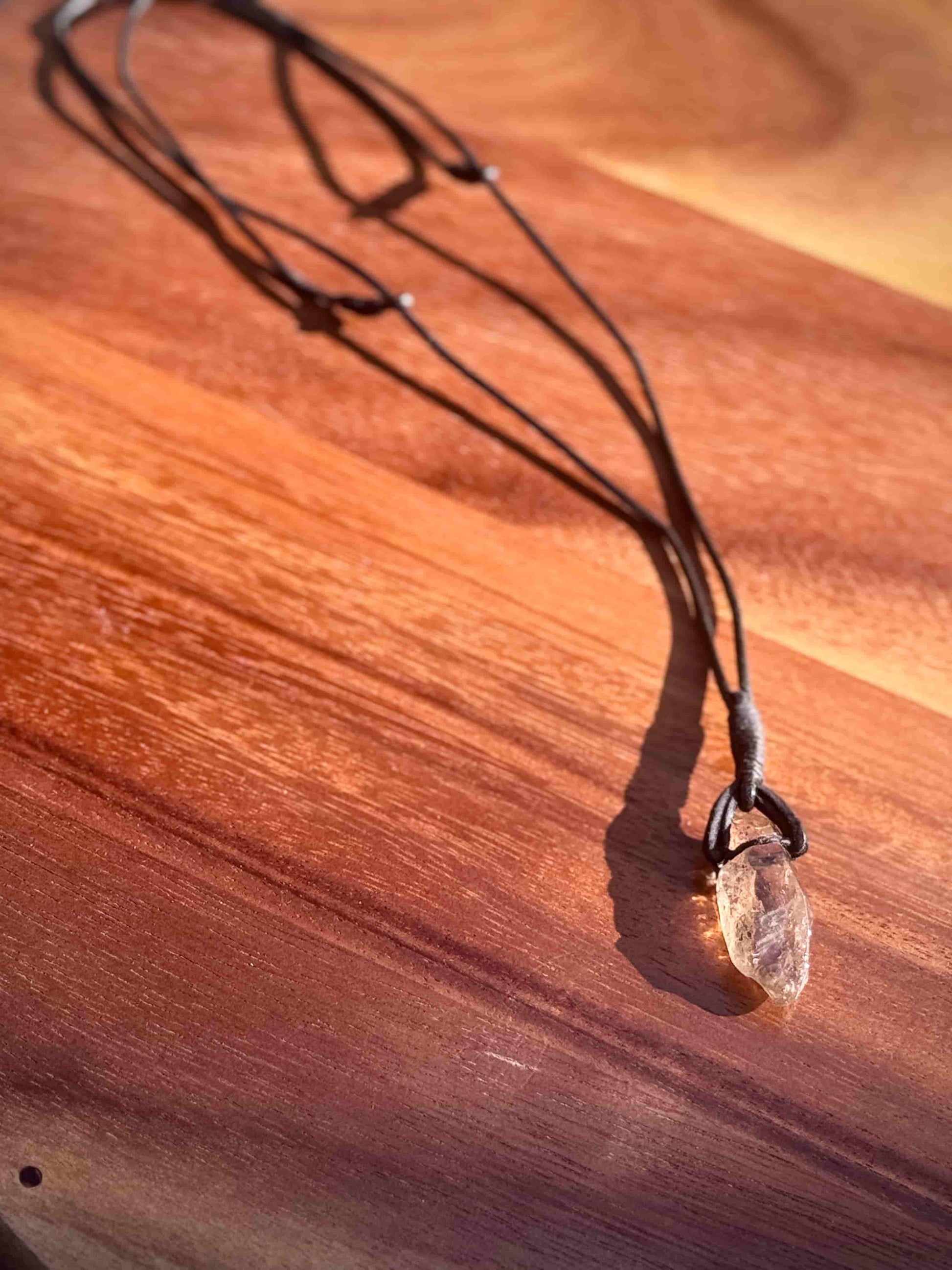 Garden Quartz stone pendant on a leather cord against a wooden table.