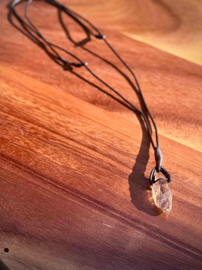 Garden Quartz stone pendant on a leather cord against a wooden table.
