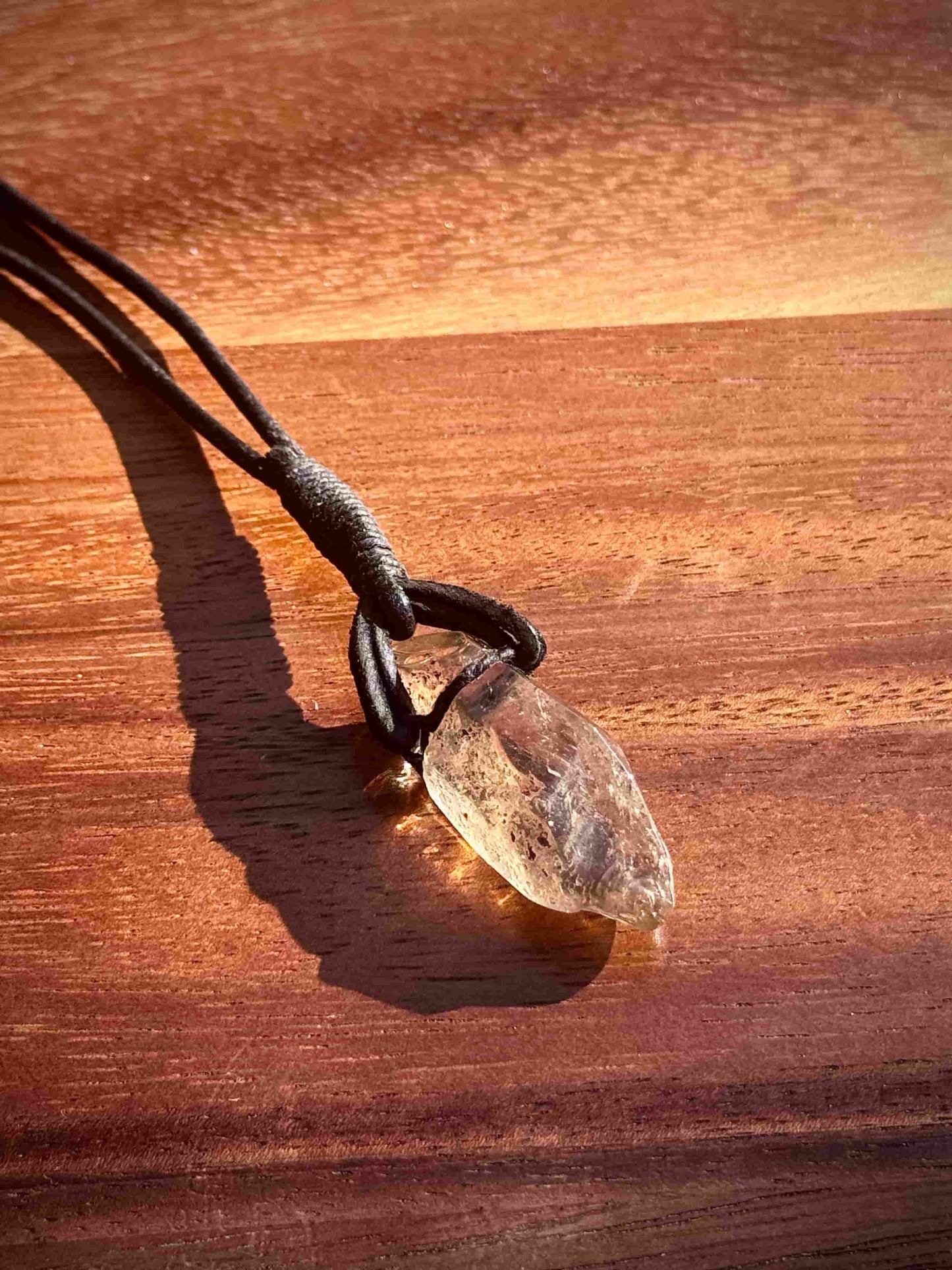 Garden Quartz stone pendant on a leather cord against a wooden background