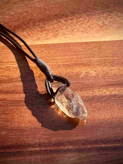 Garden Quartz stone pendant on a leather cord against a wooden background