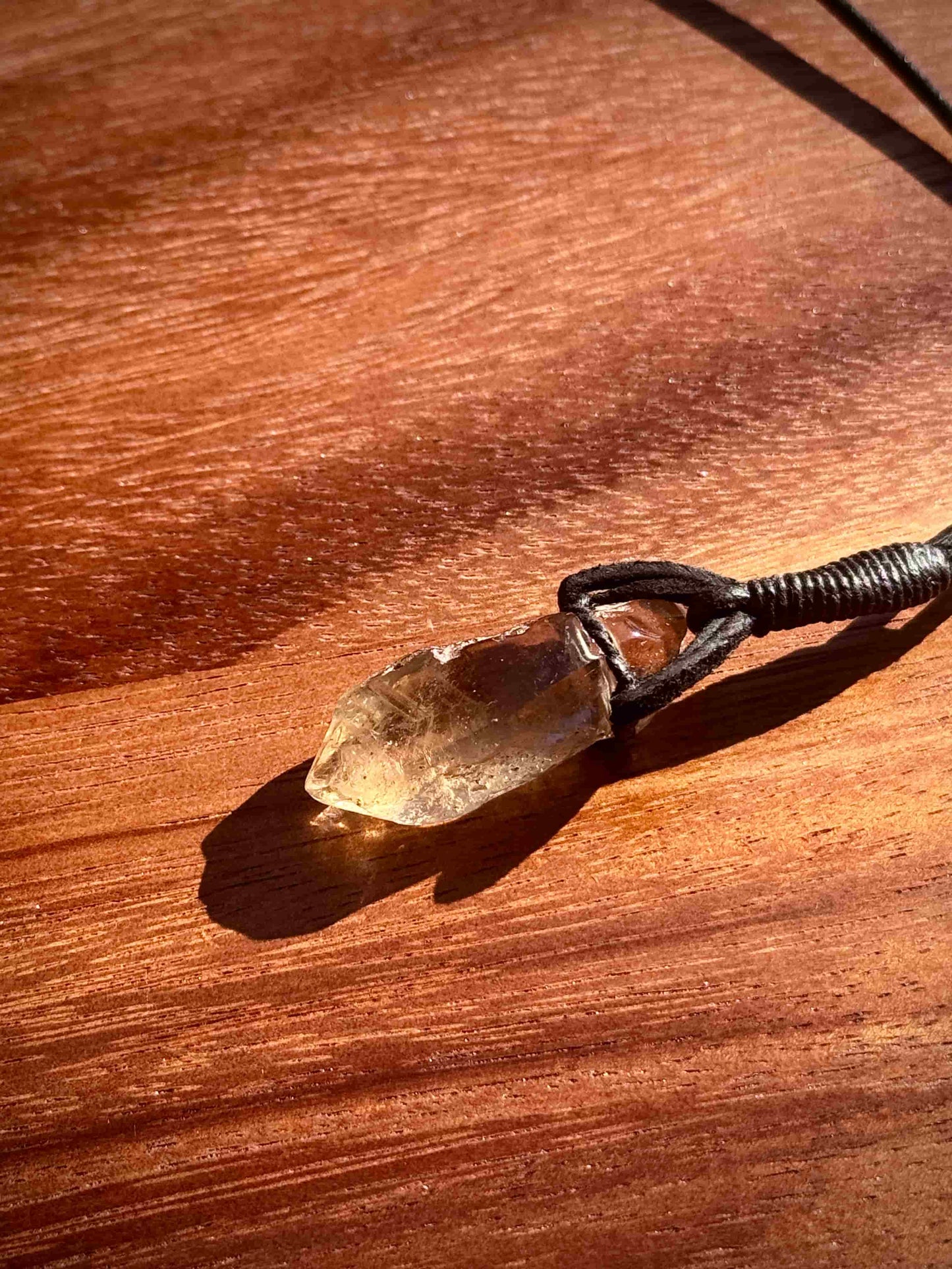 Garden Quartz stone pendant on a leather cord against a wooden background