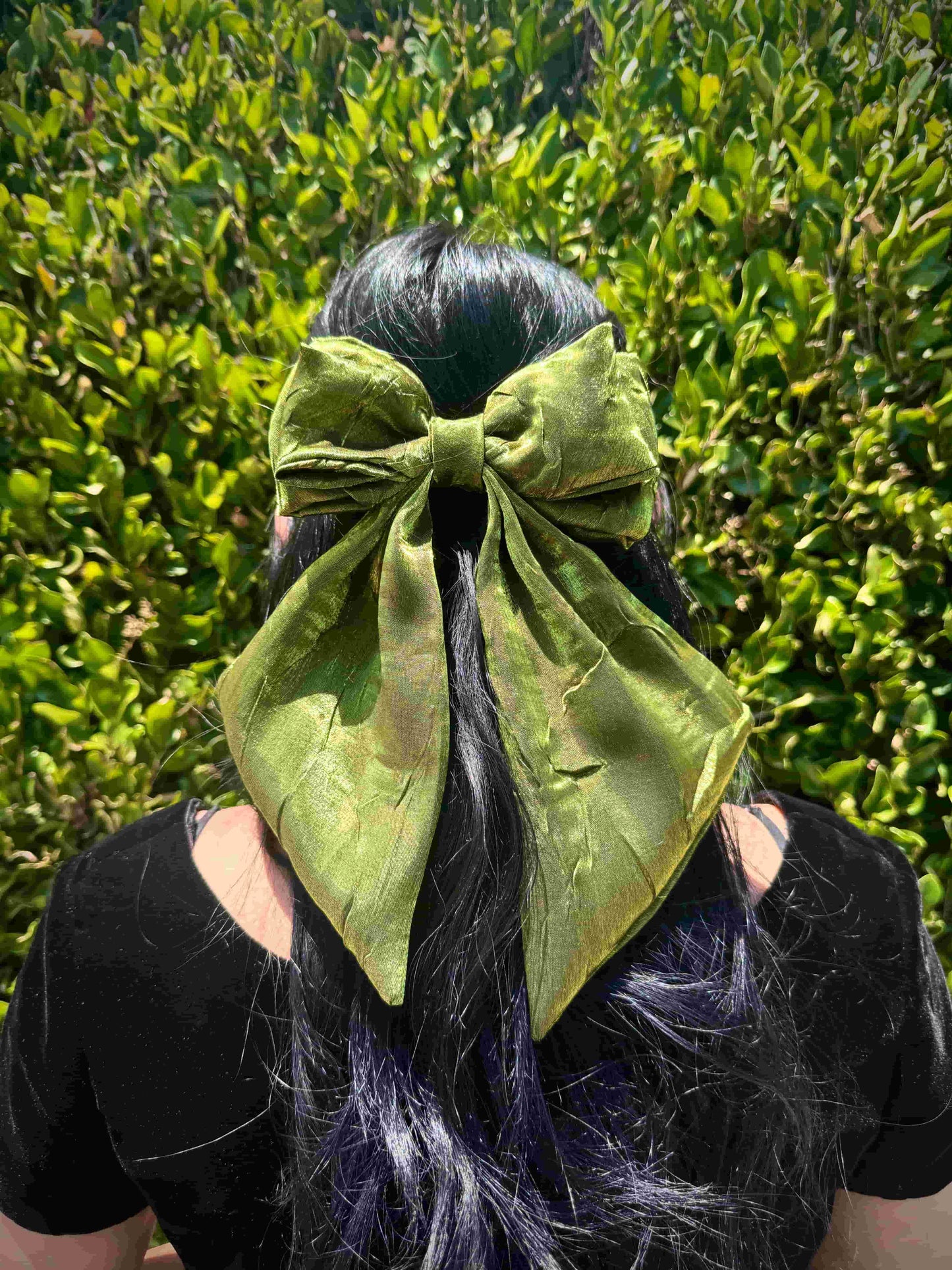 Person with green hair bow against a green leafy background