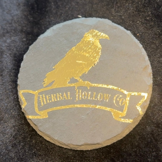Round stone coaster with gold 'Herbal Hollow Co' logo on a dark surface