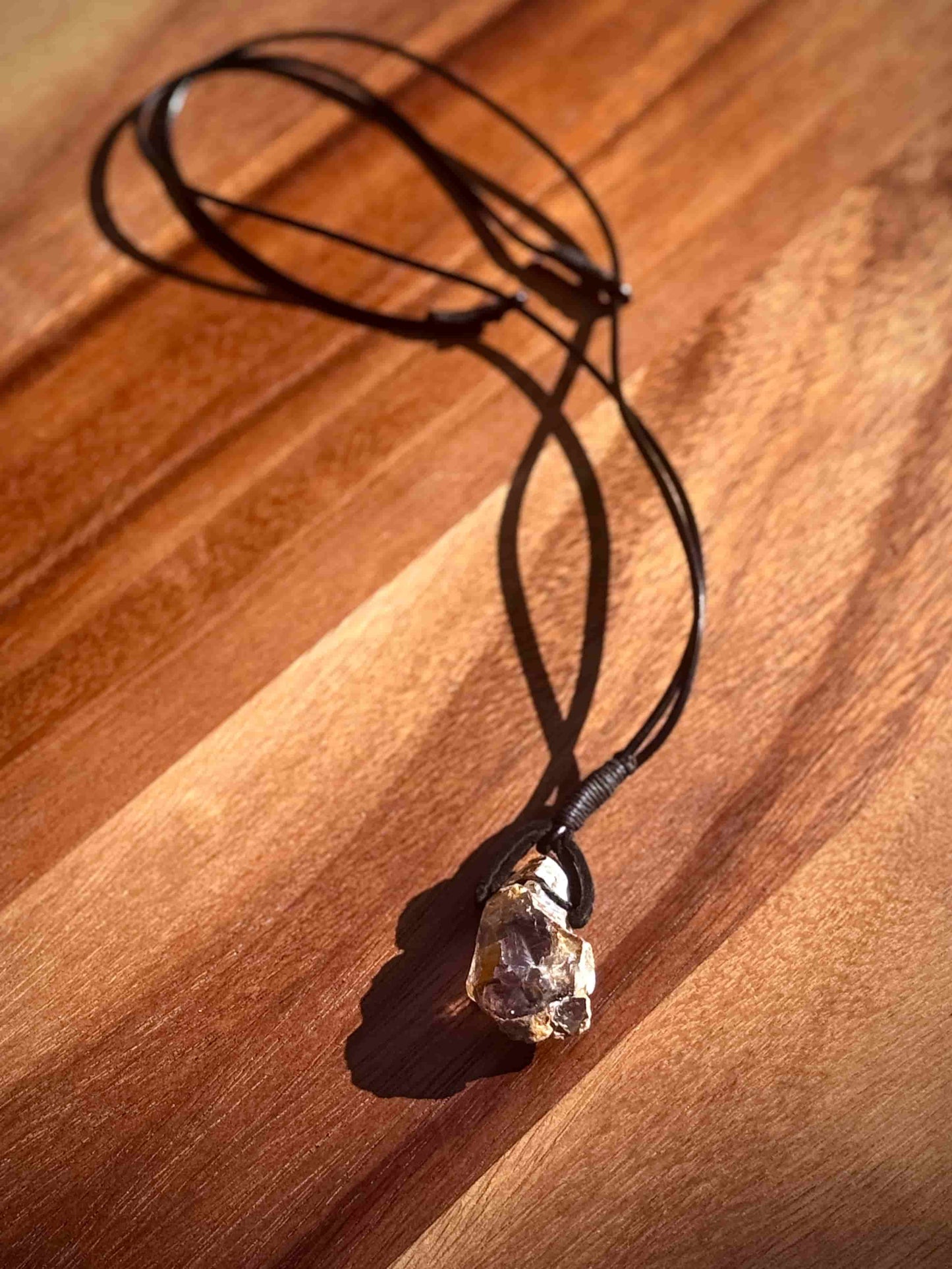 Large chunk of Garden Quartz stone pendant on a leather cord against a wooden table.