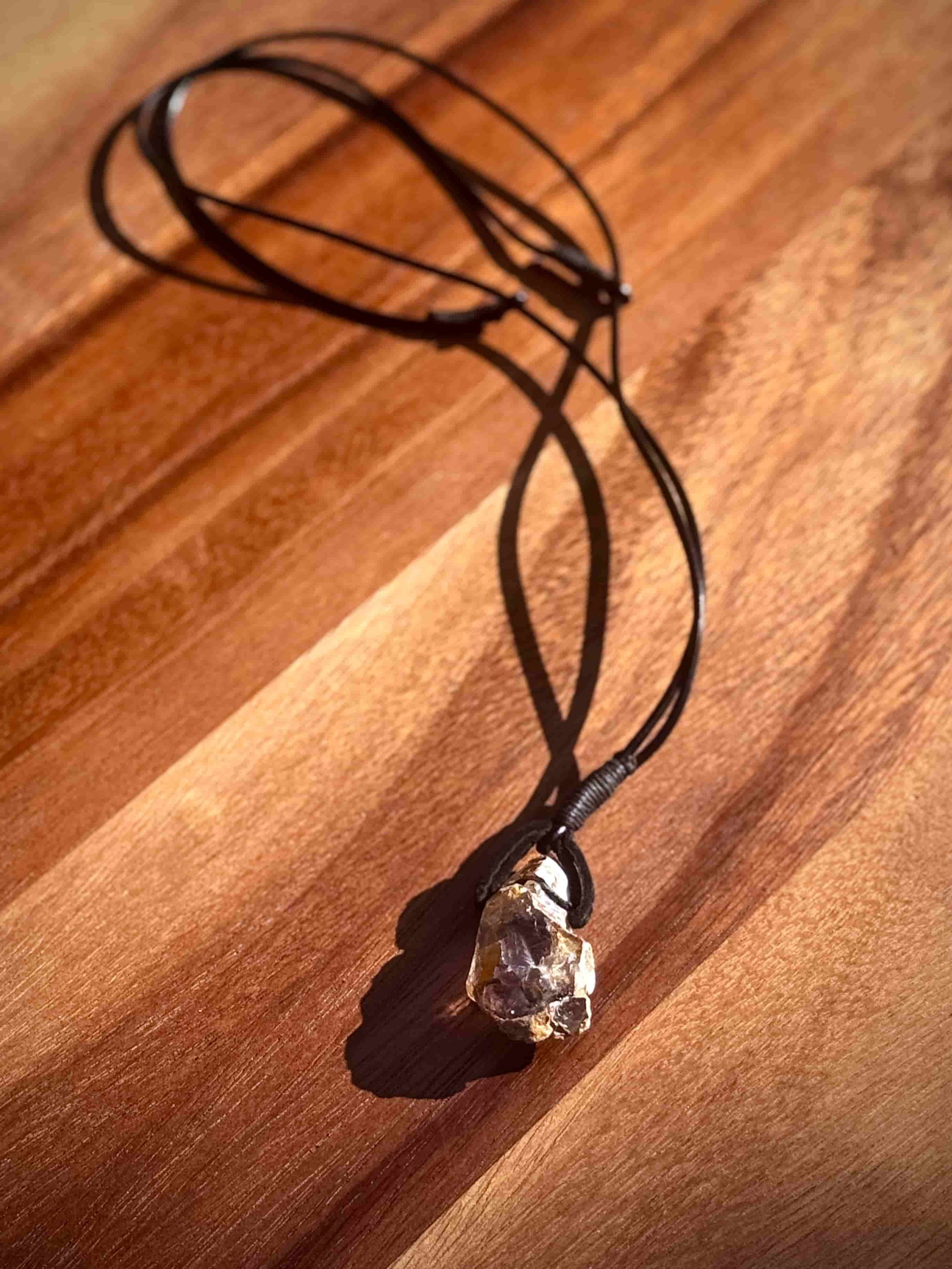 Large chunk of Garden Quartz stone pendant on a leather cord against a wooden table.