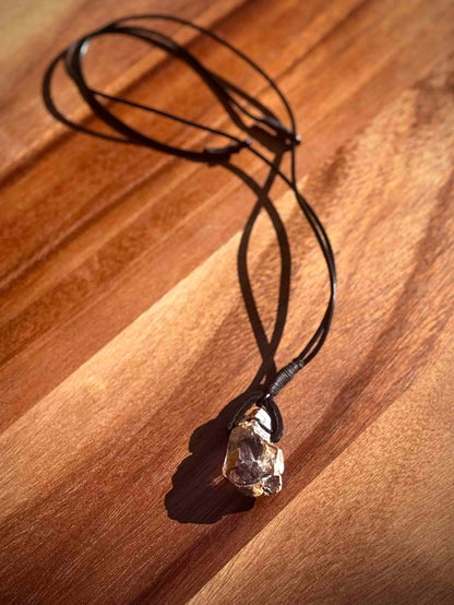 Large chunk of Garden Quartz stone pendant on a leather cord against a wooden table.