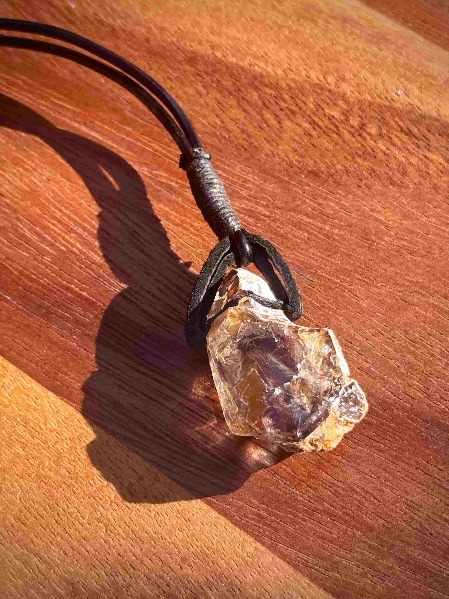 Large chunk of Garden Quartz stone pendant on a leather cord against a wooden background