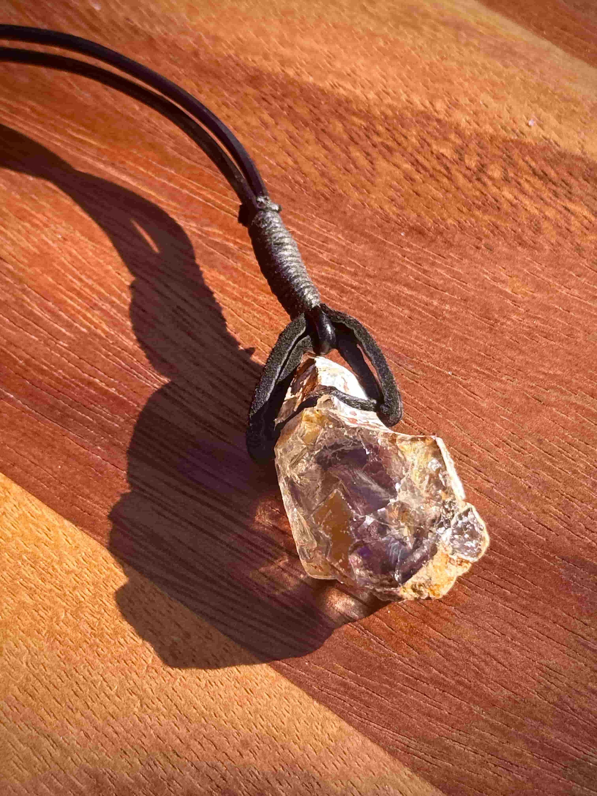 Large chunk of Garden Quartz stone pendant on a leather cord against a wooden background
