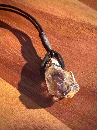 Large chunk of Garden Quartz stone pendant on a leather cord against a wooden background