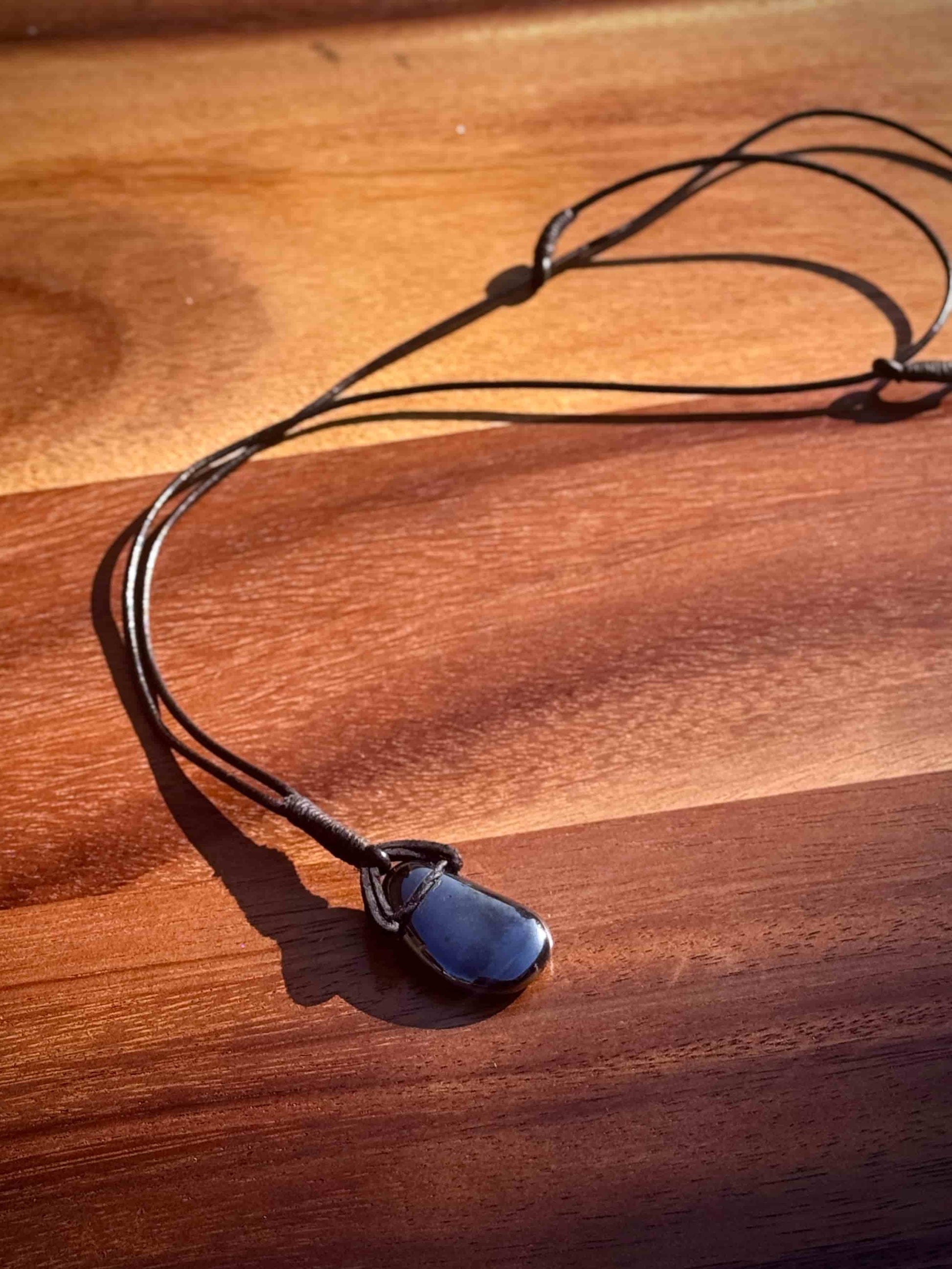 Black hematite stone pendant in a cabochon shape on a leather cord against a wooden background