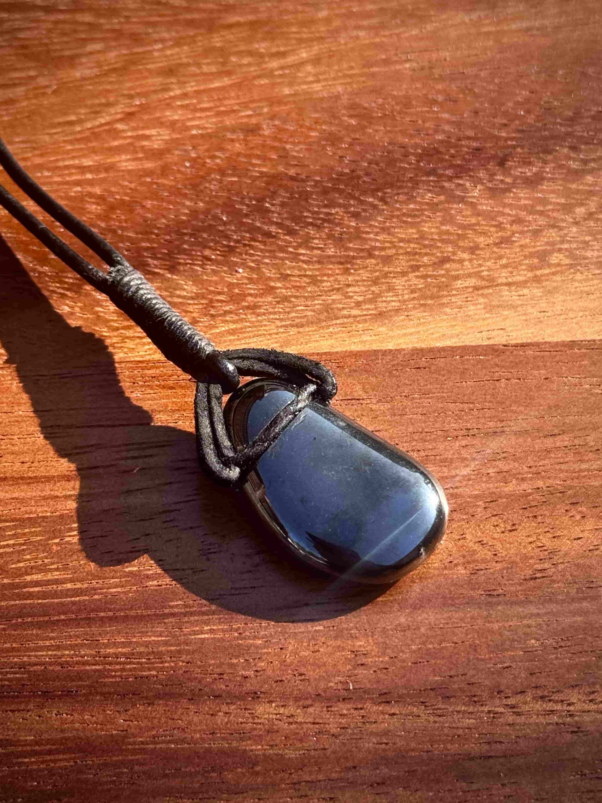 Black hematite stone pendant in a cabochon shape on a leather cord against a wooden background
