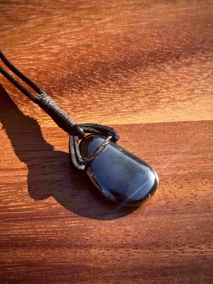 Black hematite stone pendant in a cabochon shape on a leather cord against a wooden background