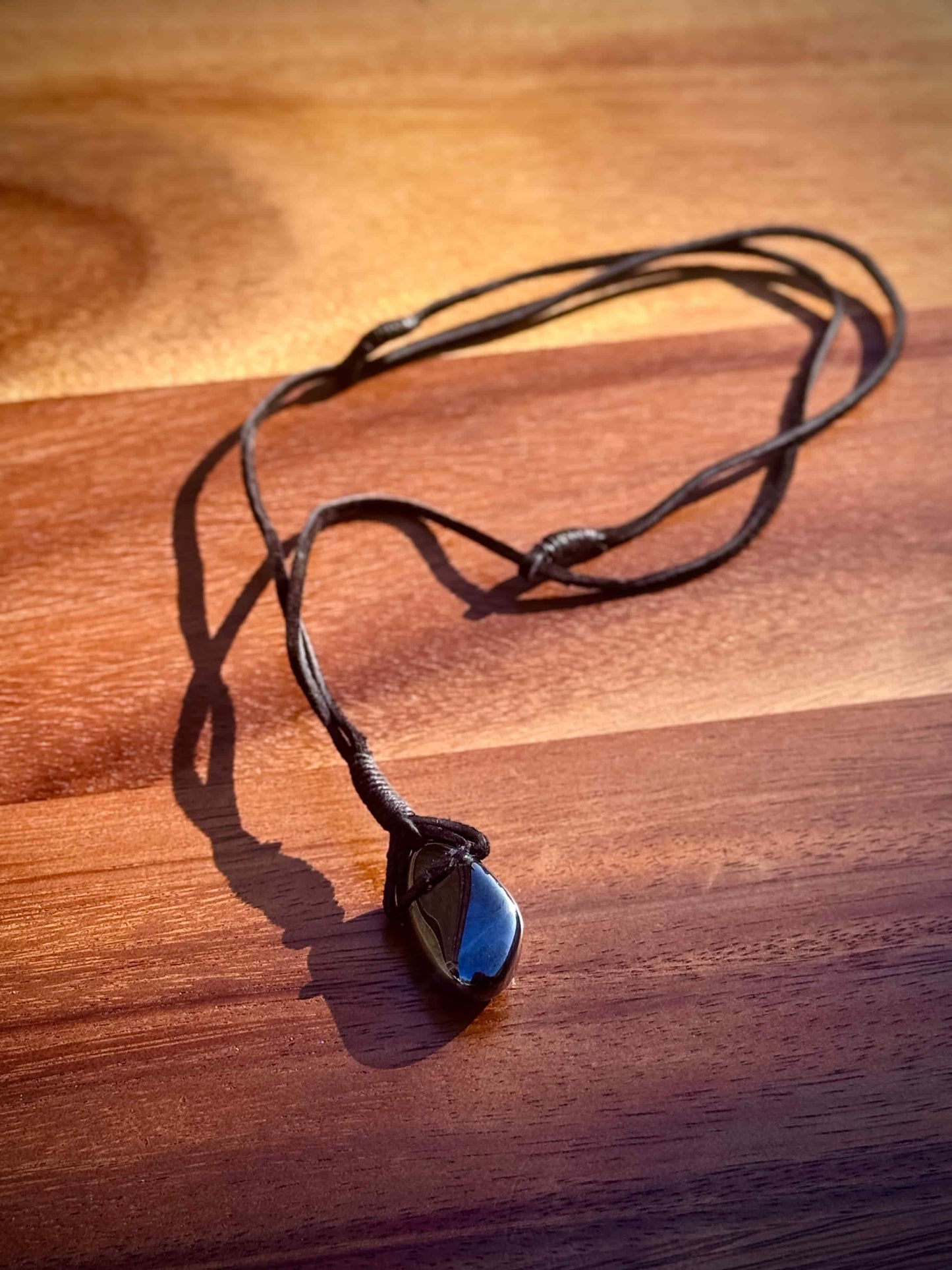 Magnetic Black Hematite stone pendant wrapped in a black leather cord against a wooden surface