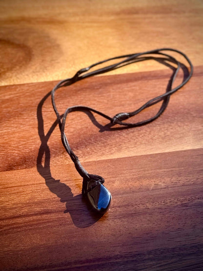 Magnetic Black Hematite stone pendant wrapped in a black leather cord against a wooden surface