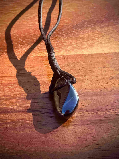 Magnetic Black Hematite stone pendant wrapped in a black leather cord against a wooden surface