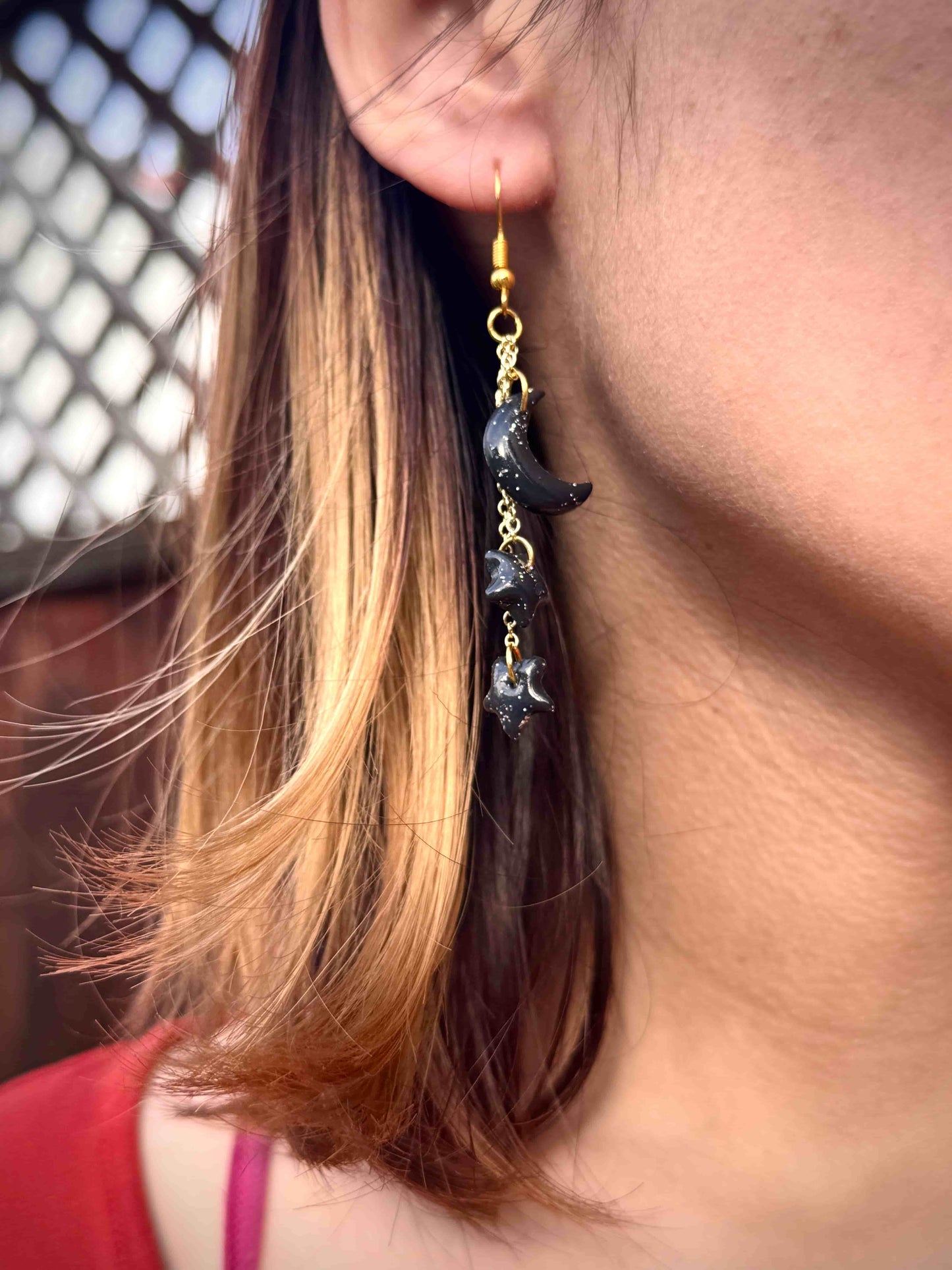 Close-up of a person wearing a dangling earring with a black crescent moon and stars and gold hook.