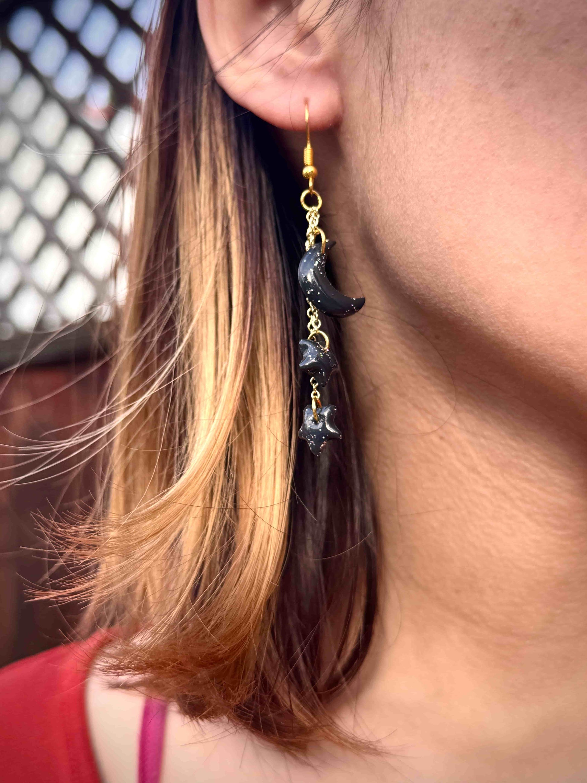 Close-up of a person wearing a dangling earring with a black crescent moon and stars and gold hook.
