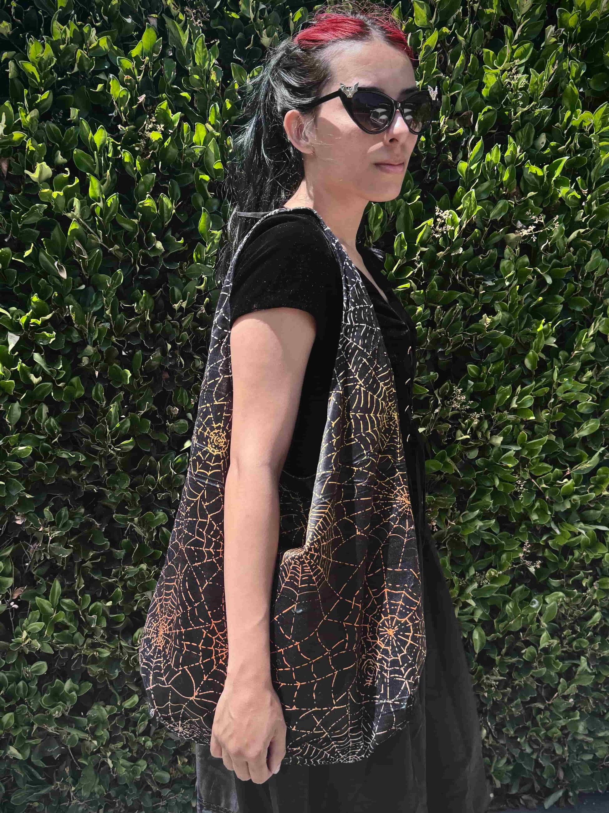 Person wearing a black and orange spiderweb patterned bag against a green hedge background