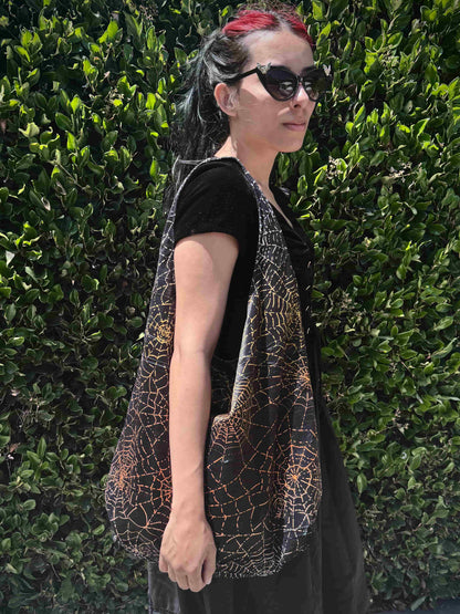 Person wearing a black and orange spiderweb patterned bag against a green hedge background