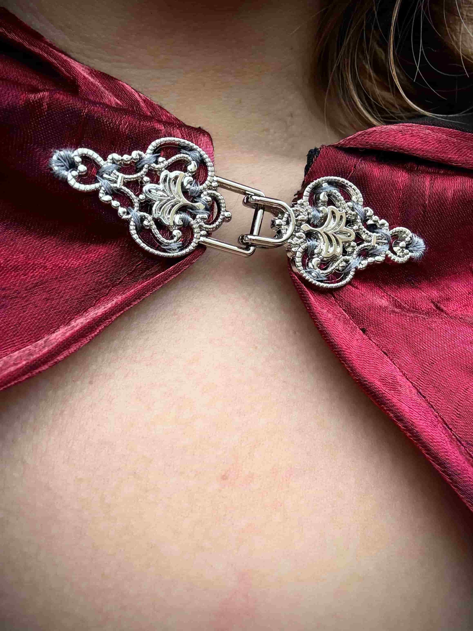 Close-up of a red cape with a decorative clasp on a person.