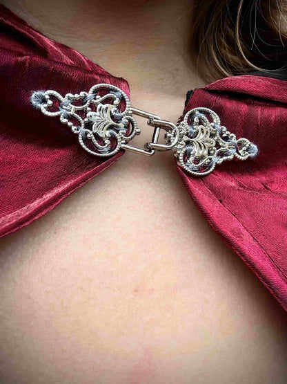 Close-up of a red cape with a decorative clasp on a person.